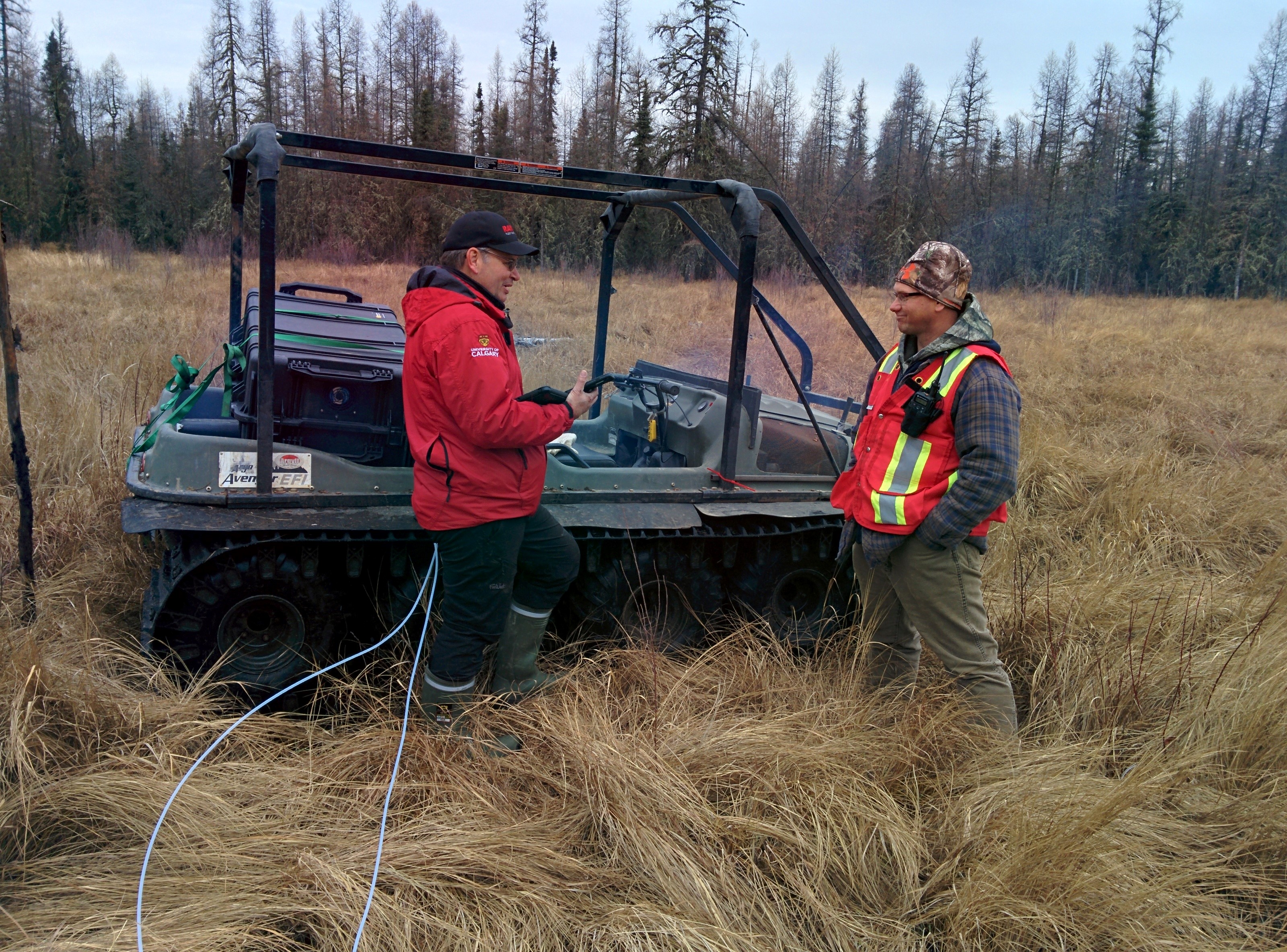 Two researchers stand beside the Argo, loaded with atmospheric leak detection technology, in a grassy, wetland in Christina Lake, Alberta.  
